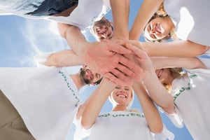 Low angle view of happy volunteers with hands together against blue sky